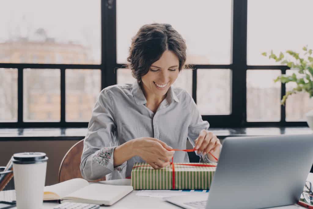 Jeune femme heureuse d'ouvrir un coffret cadeau d'entreprise à son bureau