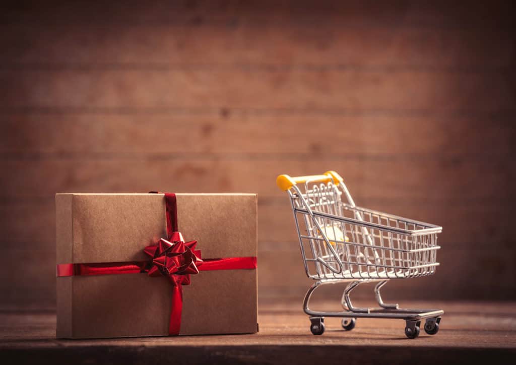 Joli paquet cadeau posé à côté d'un caddy de grande surface vide.
