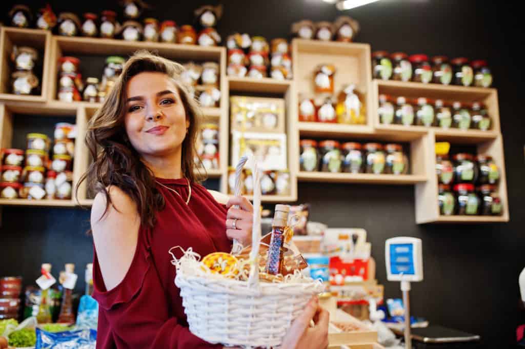Jeune femme souriante tenant un panier gourmand artisanal dans une boutique